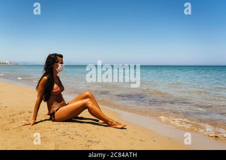 Junge Frau am Strand mit Gesichtsmaske gegen Covid oder Covid19 Stockfoto