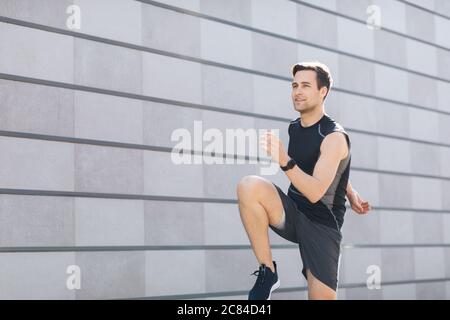 Urbaner Stil. Mann mit Fitness-Tracker geht in für Sport auf grauem Wand Hintergrund Stockfoto