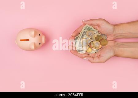 Weibliche Hände legten Geld in ein Sparschwein auf einem rosa Hintergrund. Retention für den Ruhestand. Eine Krise Stockfoto