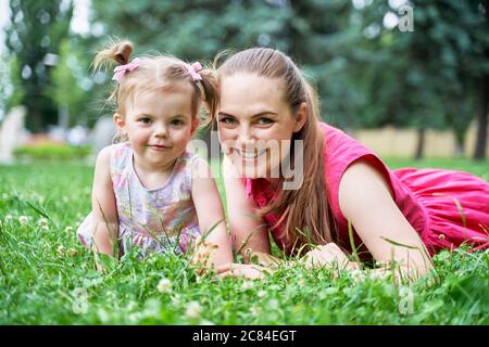 Ein kleines Mädchen mit ihrer Mutter liegt auf dem Grünes Gras und Blick in den Rahmen Stockfoto