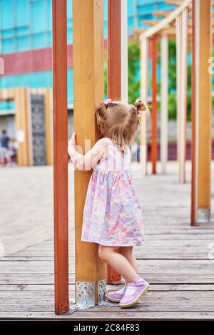 Ein kleines Mädchen mit zwei Schwänzen spielt verstecken und suchen Auf dem Spielplatz Stockfoto