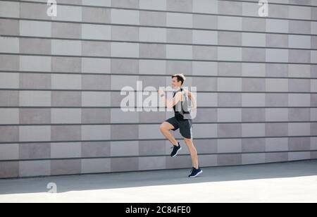 Training und Laufen in der Stadt am Morgen. Millennial man in Sportbekleidung und Fitness-Tracker läuft und springt Stockfoto