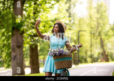Schöne schwarze Mädchen unter Selfie auf Fahrrad Fahrt im sonnigen Sommerpark Stockfoto