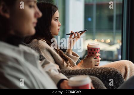 Seitenansicht des Mädchens, das Sprachnachricht auf dem Handy sendet, Kaffee trinkt in cefe Stockfoto