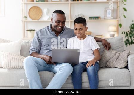 Happy Black Großvater Und Enkel Entspannen Mit Laptop Auf Der Couch Zusammen Stockfoto