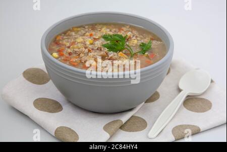 Peruanische Quinoa-Suppe mit rotem Reis und Linsen in einer grauen Tonschüssel garniert mit einem Blatt grüner Petersilie Stockfoto