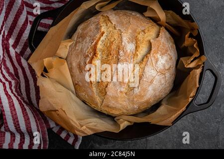 Rustikales Weißbrot in einem Gusseisen niederländischen Ofen gebacken, nur aus dem Ofen, auf einer Schieferplatte mit einem Küchentuch warten, um zu kühlen platziert Stockfoto