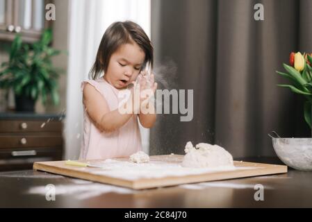 Schöne kleine Mädchen klatscht Hände mit Mehl. Kind spielt mit Mehl in der Küche Stockfoto