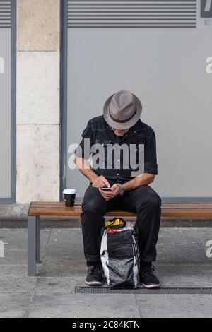 Schwarz gekleideter Mann, der sein Handy benutzte, während er in Basel auf eine Straßenbahn wartete Stockfoto