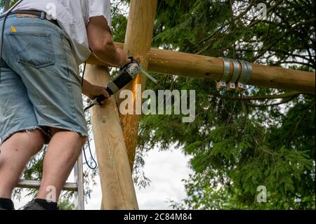 Ein Arbeiter benutzt einen Schleifer, um eine Schaukel in einem privaten Garten zu bauen. Stockfoto