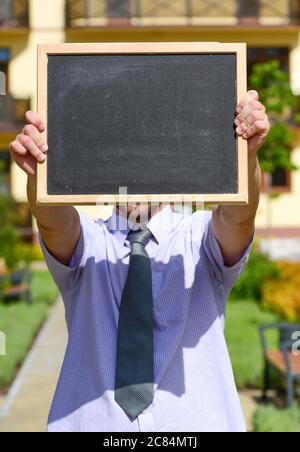 Business und Immobilien Konzept. Immobilienmakler hält Tafel oder Tafel vor seinem Gesicht, Platz kopieren. Verkäufer oder Geschäftsmann mit Werbung für Verkauf. Geschäftsmann mit Gebäude im Hintergrund Stockfoto