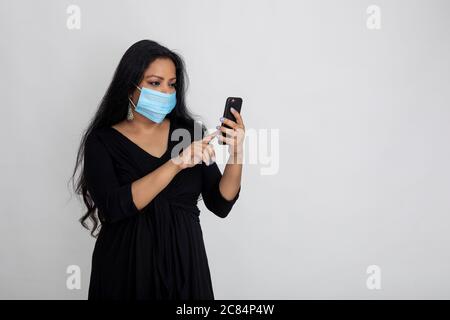 Indische Frau trägt Covid Schutzmaske, Lady mit ihrem Telefon Stockfoto