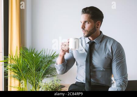 Junger Geschäftsmann, der in seinem Büro arbeitet und Kaffee trinkt Stockfoto