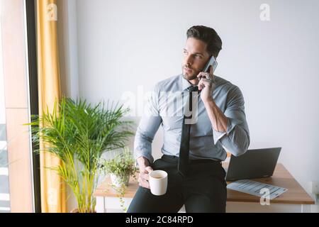 Junger Geschäftsmann, der in seinem Büro arbeitet und Kaffee trinkt Stockfoto