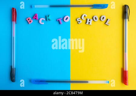 Rahmen aus mehrfarbigen Kugelschreibern auf gelbem und blauem Hintergrund. Inschrift aus farbigen Buchstaben zurück zur Schule. Flach liegend, Platz für Text, Stockfoto