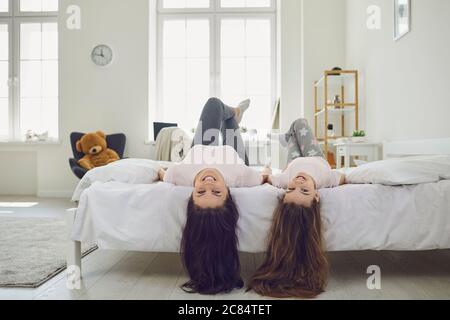 Fröhliche Mutter und Tochter mit schönen Haaren, die Kopf nach unten auf dem Bett zu Hause liegen. Eltern und Kinder haben Spaß im Schlafzimmer Stockfoto