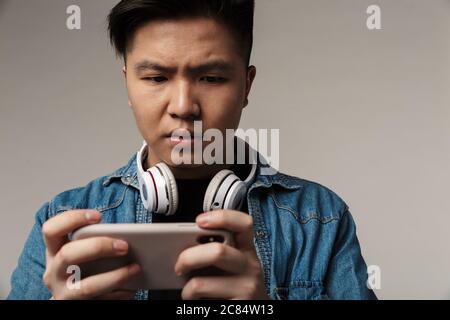 Bild von fokussierten jungen asiatischen Mann spielen Videospiel auf Smartphone isoliert über grauen Hintergrund Stockfoto