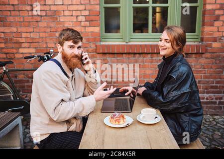 Junges Paar arbeitet freudig zusammen während der Kaffeepause im Straßencafé Stockfoto