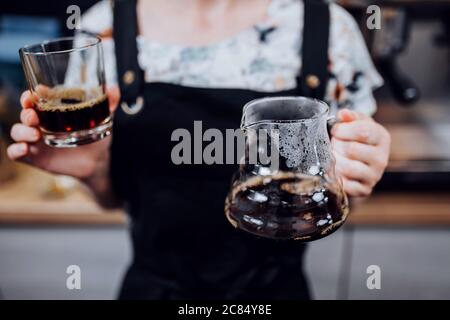 Ein Glas Kaffee, zubereitet nach einer Tropfmethode in den weiblichen Händen eines Barista Stockfoto