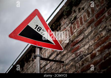 Straßenschild an einer alten Ziegelmauer, die vor einer Steigung warnt Stockfoto