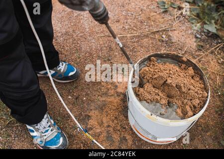 Vorbereitung des Zementleimörtels in einem Eimer aus Zement und Sand mit einer Mischdüse auf einem Bohrer - die Arbeit eines professionellen Maurer Stockfoto