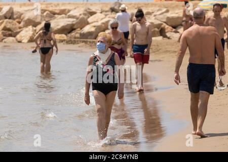 Torrenostra, Castellón, Spanien - 19. Juli 2020: Eine ältere Frau, Rentnerin, geht mit einer Maske am Strand entlang, um die Ausbreitung von COVID-19 zu verhindern. Stockfoto