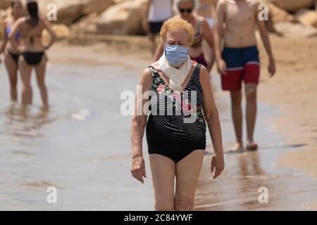 Torrenostra, Castellón, Spanien - 19. Juli 2020: Eine ältere Frau, Rentnerin, geht mit einer Maske am Strand entlang, um die Ausbreitung von COVID-19 zu verhindern. Stockfoto