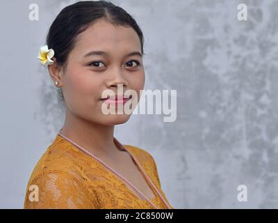 Die junge Balinesin trägt eine Frangipani (Plumeria) Blume im Haar und posiert für die Kamera. Stockfoto