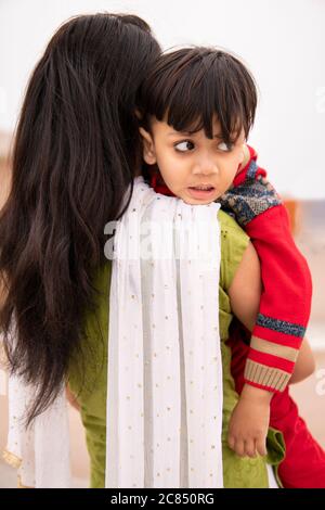 Rückansicht einer Tante, die ihren geschnittenen kleinen Neffen im Freien hält. Sie trägt traditionelle indische Kleidung Salwar Kameez und Dupatta. Stockfoto