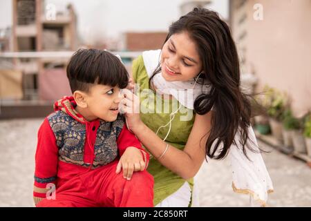 Rückansicht einer Tante, die ihren geschnittenen kleinen Neffen im Freien hält. Sie trägt traditionelle indische Kleidung Salwar Kameez und Dupatta. Stockfoto