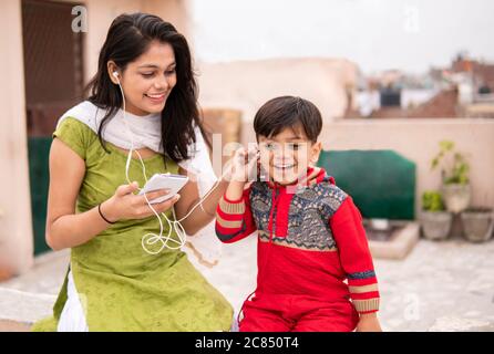 Rückansicht einer Tante, die ihren geschnittenen kleinen Neffen im Freien hält. Sie trägt traditionelle indische Kleidung Salwar Kameez und Dupatta. Stockfoto