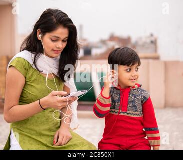 Rückansicht einer Tante, die ihren geschnittenen kleinen Neffen im Freien hält. Sie trägt traditionelle indische Kleidung Salwar Kameez und Dupatta. Stockfoto