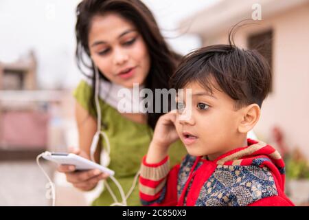 Rückansicht einer Tante, die ihren geschnittenen kleinen Neffen im Freien hält. Sie trägt traditionelle indische Kleidung Salwar Kameez und Dupatta. Stockfoto