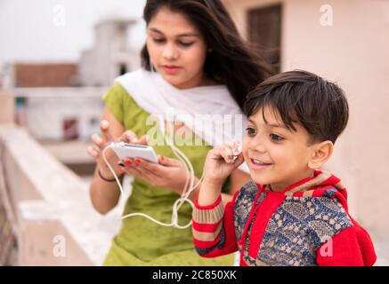 Rückansicht einer Tante, die ihren geschnittenen kleinen Neffen im Freien hält. Sie trägt traditionelle indische Kleidung Salwar Kameez und Dupatta. Stockfoto