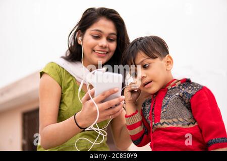 Rückansicht einer Tante, die ihren geschnittenen kleinen Neffen im Freien hält. Sie trägt traditionelle indische Kleidung Salwar Kameez und Dupatta. Stockfoto