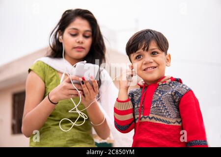 Rückansicht einer Tante, die ihren geschnittenen kleinen Neffen im Freien hält. Sie trägt traditionelle indische Kleidung Salwar Kameez und Dupatta. Stockfoto