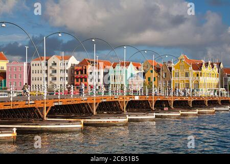 Menschen, die über Queen Emma Swing Bridge mit typisch holländischen Gebäuden im Hintergrund, Willemstat, Curacao, Karibik, West Indies Stockfoto