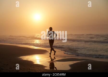 Ein Mann, der am Morgen entlang der Küste des Meeres läuft Stockfoto