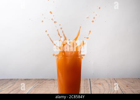 Orangensaft wird aus einem Glas gesprüht. Sprühen Sie ein süßes Getränk. Ein Spritzer Fruchtsaft. Stockfoto