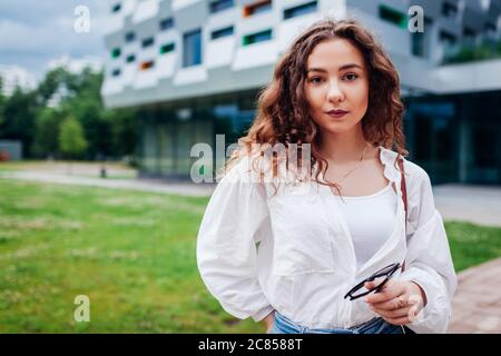 Junge Frau zu Fuß in der Stadt durch moderne Architektur im Park. Mädchen tragen stilvolle Outfit Stockfoto