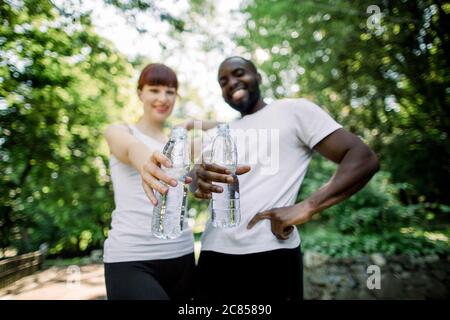 Zwei lächelnde junge multirassische Freunde, Afrikaner und Kaukasische Frau, posieren vor der Kamera nach dem Joggen Training im Freien im Stadtpark, zeigen Stockfoto