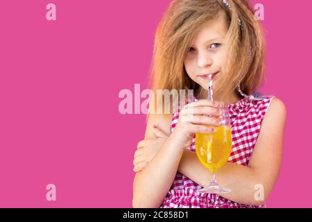 Kleine blonde Mädchen in rot kariert Kleid trinken Saft, isoliert auf rosa Hintergrund Stockfoto