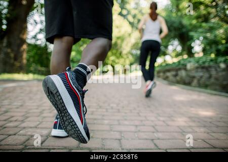 Close up Rückansicht Foto von Beinen des afrikanischen Mannes in Sport-Sneakers Joggen im Stadtpark an einem sonnigen Sommertag, zusammen mit seiner weiblichen Kaukasier Stockfoto