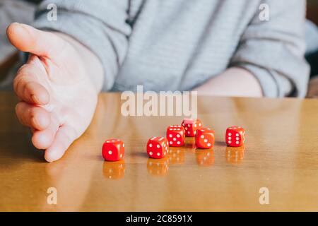 Weibliche Hand, die sechs rote Würfel auf den Tisch wirft. Yamb, Würfelspiel Stockfoto