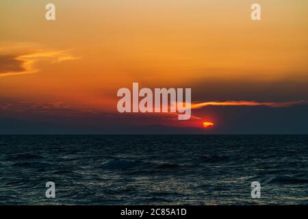 Schöner, farbenfroher Sonnenuntergang am Meer mit dramatischen Wolken und Bergen Stockfoto