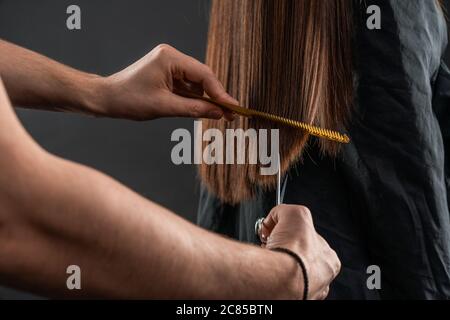 Der Friseur schneidet die Haarspitzen einer Brünette, die in einem Schönheitssalon sitzt Stockfoto