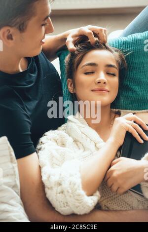 Die kaukasische Frau mit einem weißen Strickpullover liegt mit geschlossenen Augen auf ihrem Freund Stockfoto