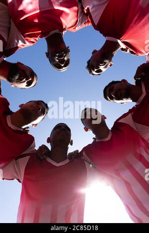 Low-Winkel-Ansicht der multi ethnischen Team von männlichen fünf ein Seite Fußballspieler tragen eine Mannschaftsstreifen Training auf einem Sportplatz in der Sonne, im Huddl stehen Stockfoto