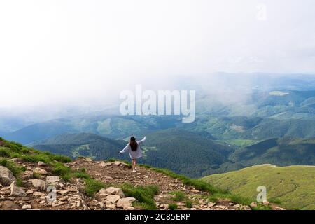 Das Mädchen steht auf dem Berg und genießt den Blick auf das Tal. Bei der Morgendämmerung, Hände hoch Stockfoto