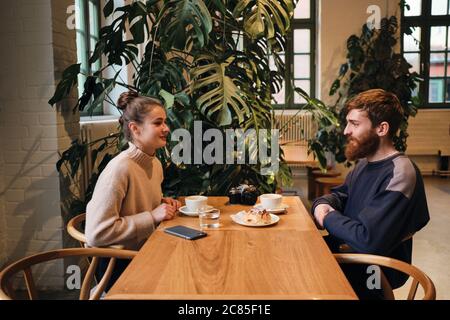 Seitenansicht des jungen schönen Paares, das sich beim Kaffee im Café verträumt anschaut Stockfoto